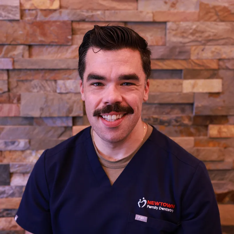 Dr. Colin of Newtown Family Dentistry smiling in navy scrubs