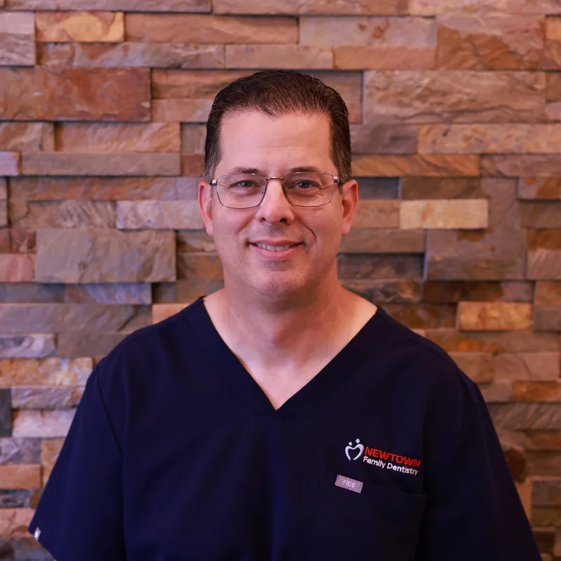 Dr. Mark of Newtown Family Dentistry smiling in navy scrubs